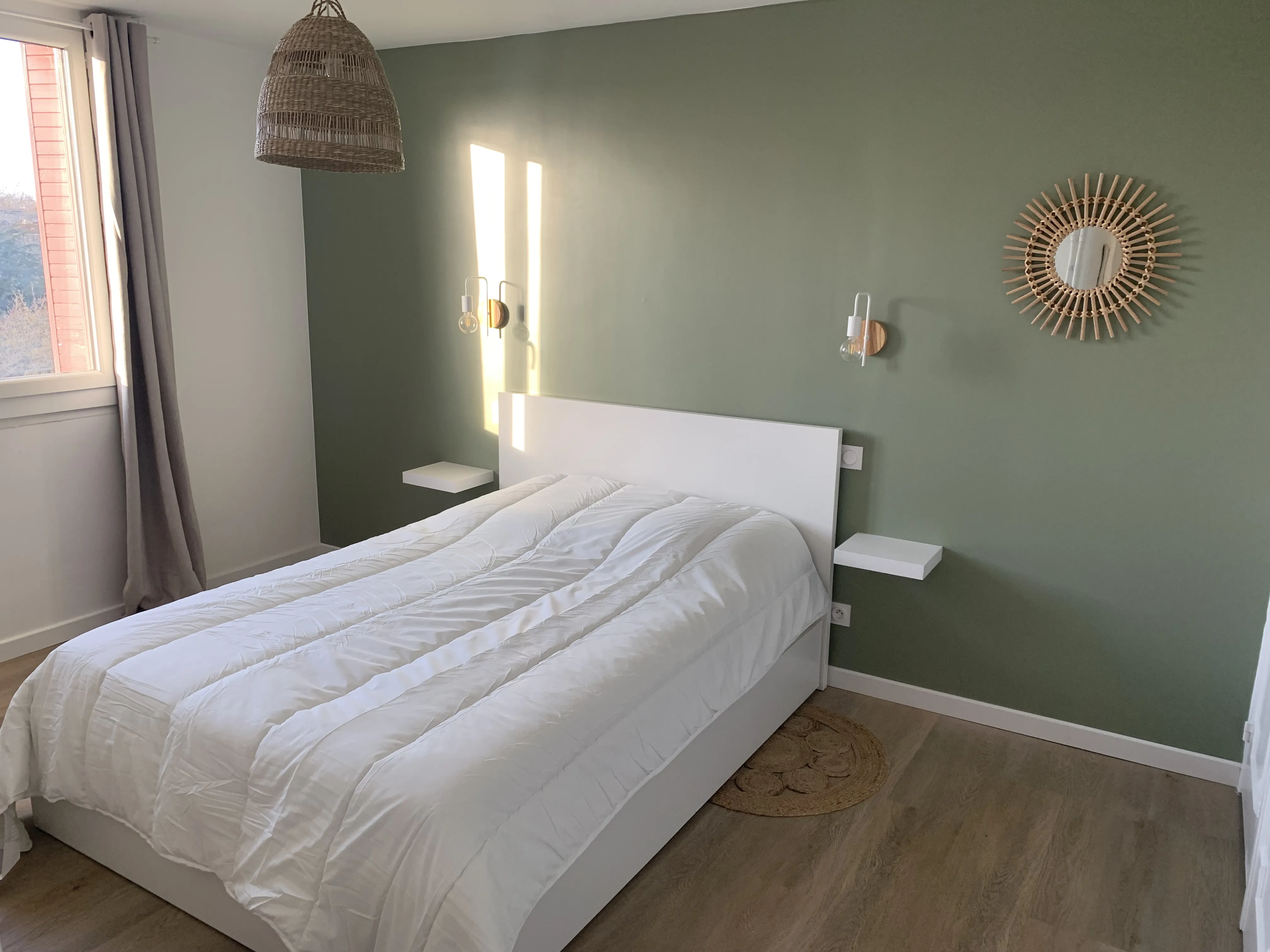 Lit double avec mur vert sauge, tablettes et miroir en rotin